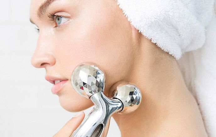 A girl uses a mechanical massager to rejuvenate her facial skin. 